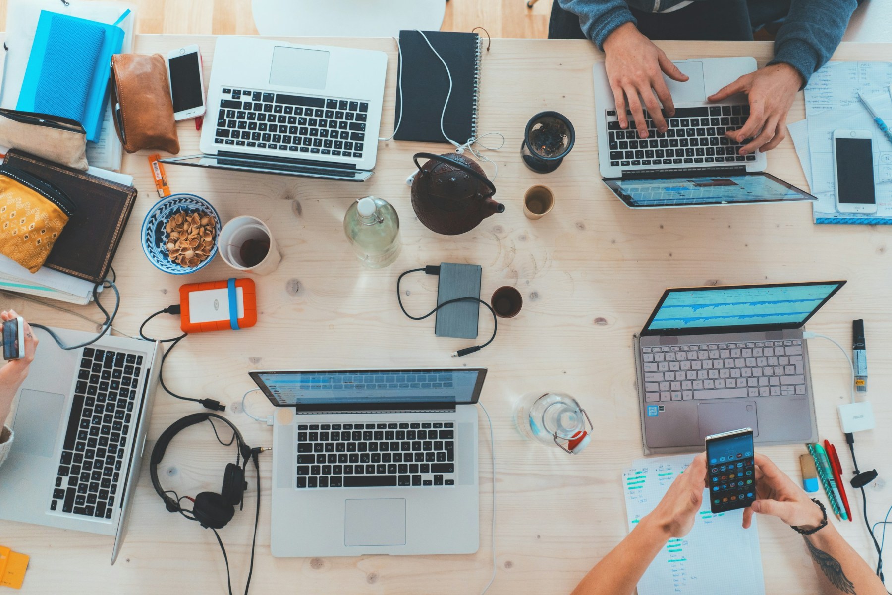 Team von oben am Schreibtisch mit Laptops, Notizbüchern und Smartphones